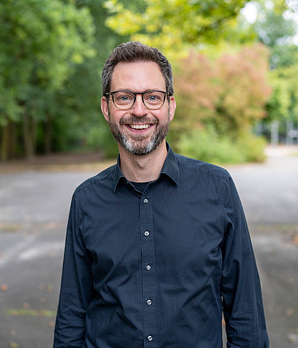 Lehrer mit Brille lächelt vor parkähnlichem Hintergrund
